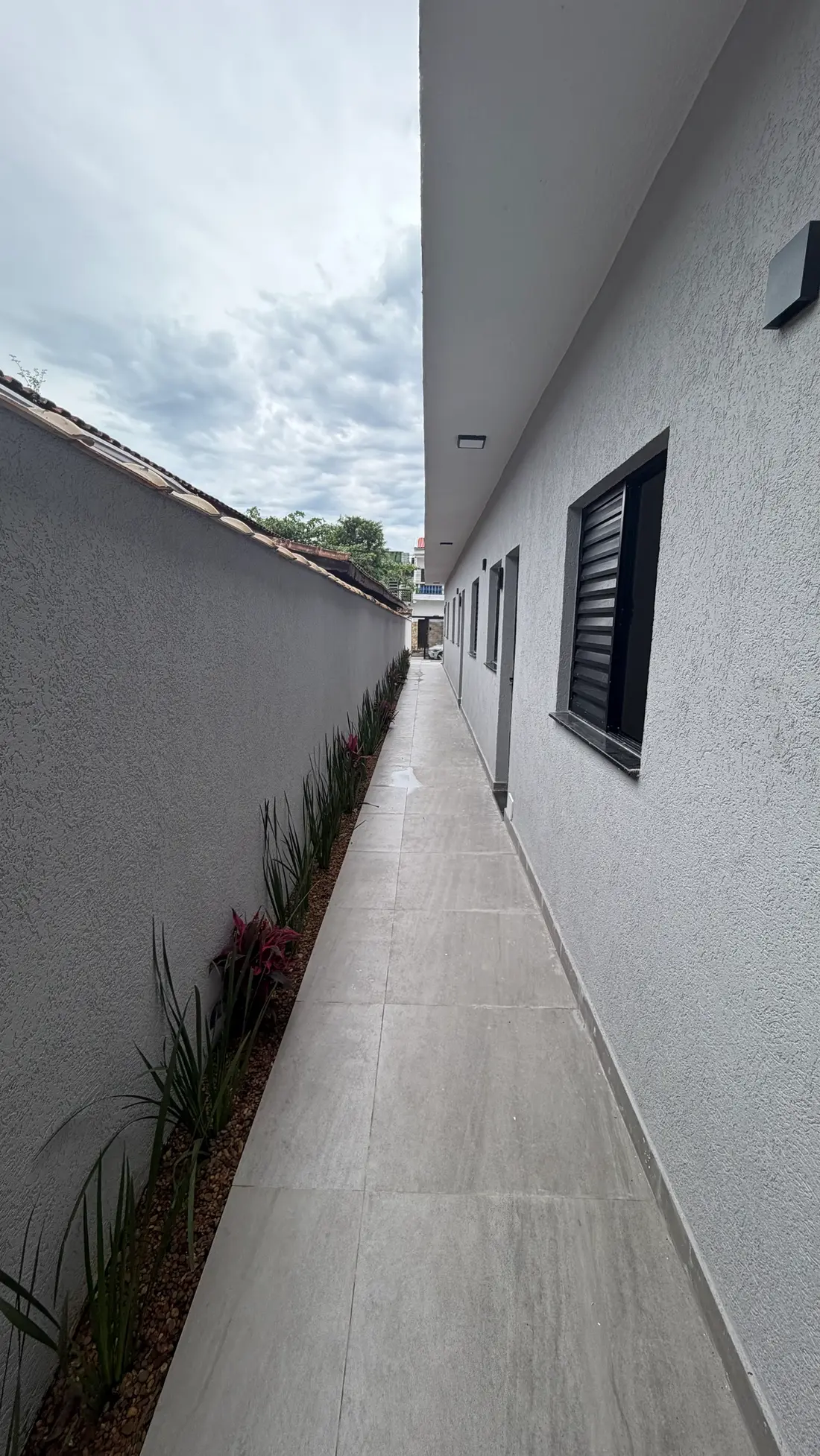Corredor lateral com piso porcelanato, jardim e janelas das casas